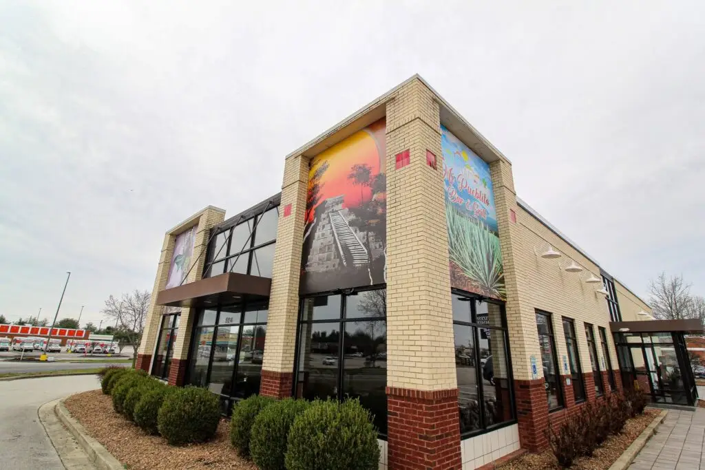 Exterior view of the brick building for Mi Pueblito Bar and Grill featuring large decorative wall murals and glass windows.
