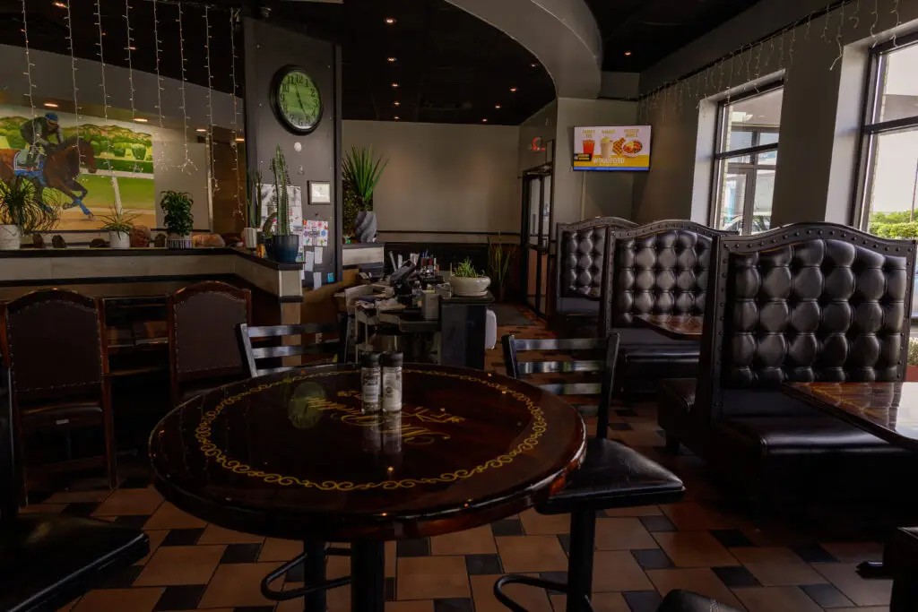 Interior dining area of a restaurant featuring round wooden tables, high-backed black tufted booths, and large windows.