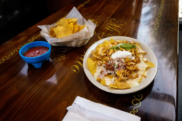 A plate of loaded chicken nachos topped with guacamole and sour cream, served with chips and salsa on a wooden table.